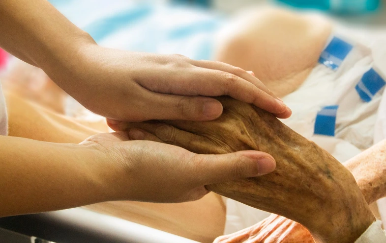 A young person gently holds the hand of an elderly individual, symbolizing care and connection across generations.