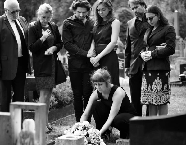 A family gathered in mourning at a cemetery, supporting each other as part of the funeral arrangements.