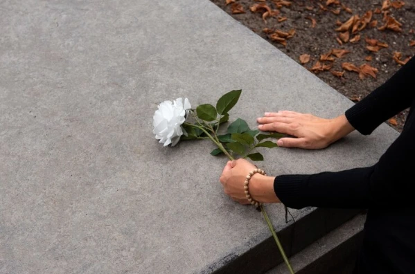 A person placing a single white rose on a grave, a heartfelt part of funeral arrangements to honor a loved one.