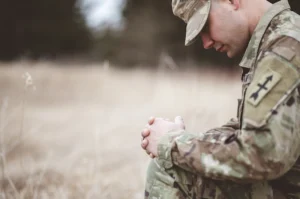 A young soldier in uniform kneeling in prayer, symbolizing hope and resilience. Veteran foundation offering support for mental health and well-being.