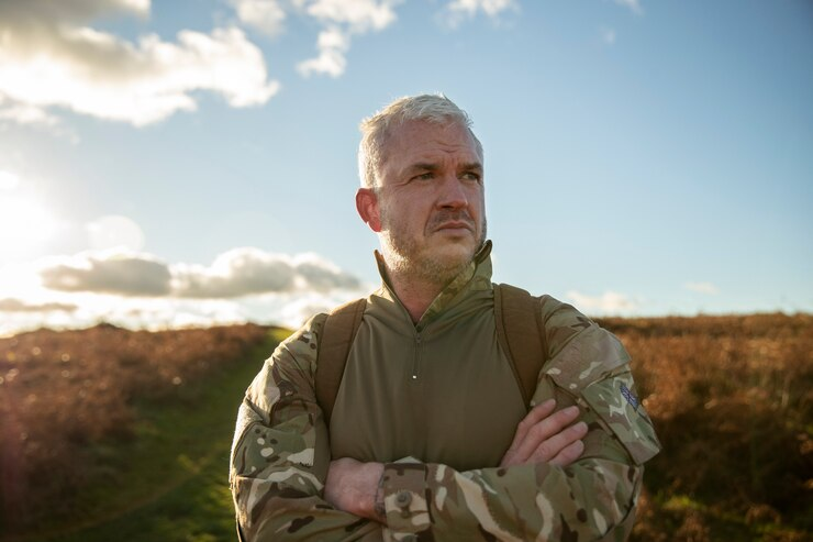 A determined older veteran in military gear standing with arms crossed, looking into the distance. A veteran foundation dedicated to post-service support and reintegration.