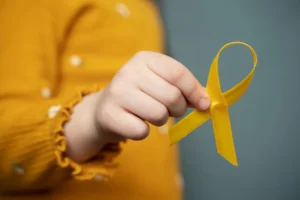 A child's hand holding a yellow ribbon, symbolizing childhood cancer awareness and hope.