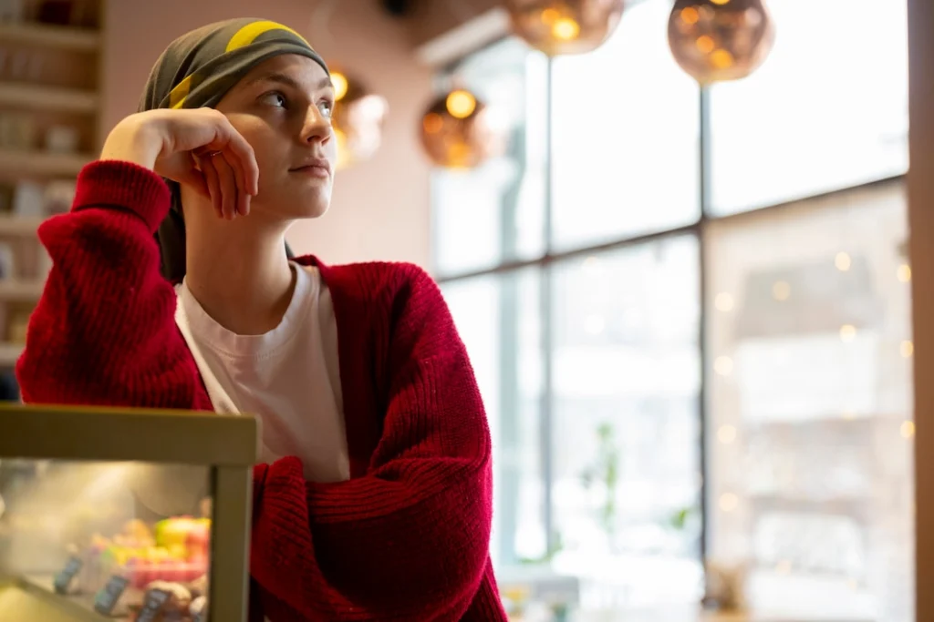 A young woman wearing a headscarf and red sweater, looking thoughtful in a cozy café, representing resilience and support for women in Los Angeles.