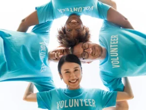 Diverse group of volunteers in blue T-shirts smiling in a circle, representing unity and teamwork—skills you gain as a volunteer.